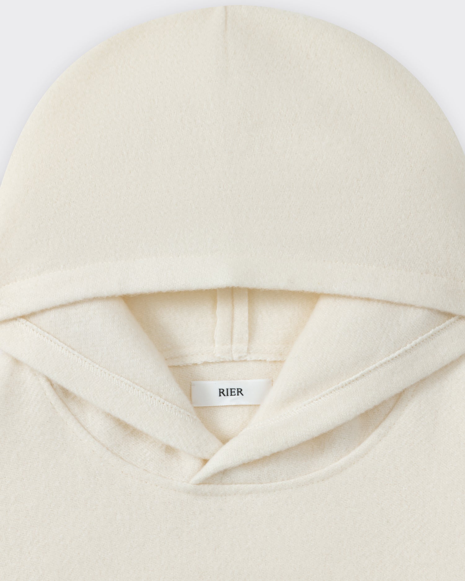 RIER hooded wool fleece in white, close-up of the hood and woven label