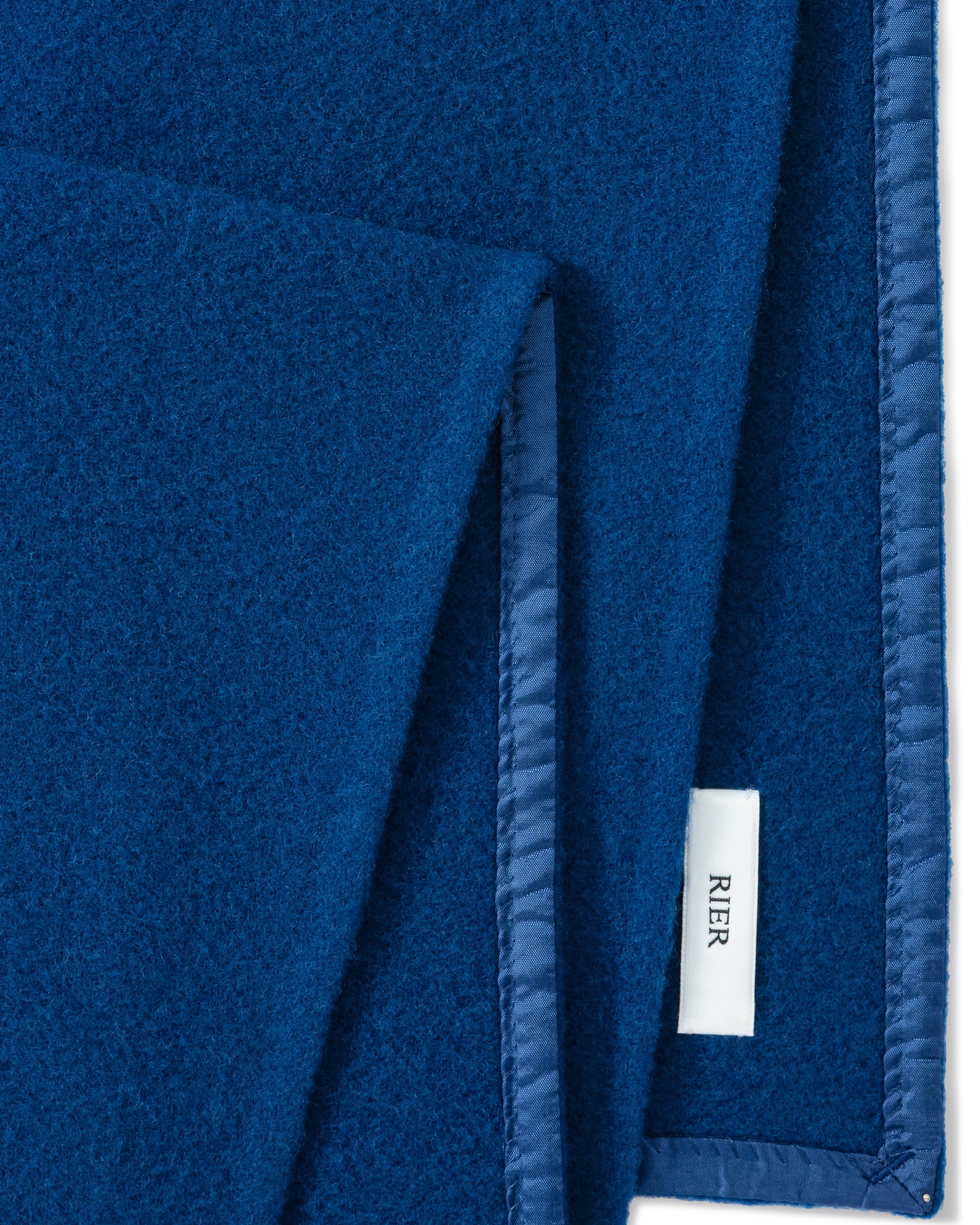 RIER wool fleece scarf in indigo blue, close-up of the finished edge and woven label