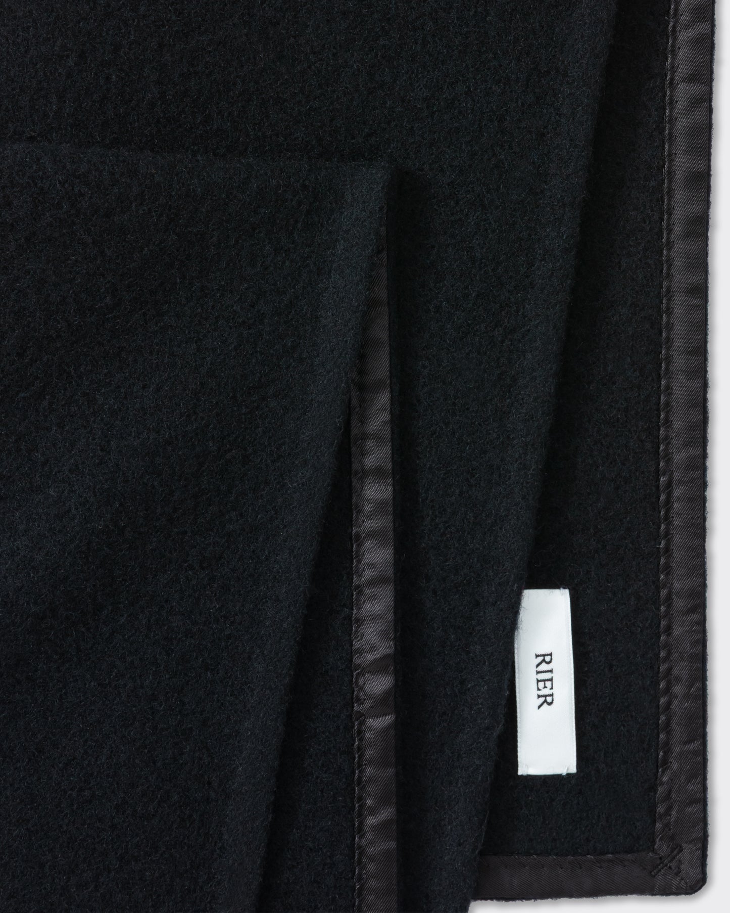 RIER wool fleece scarf in black, close-up of the finished edge and woven label