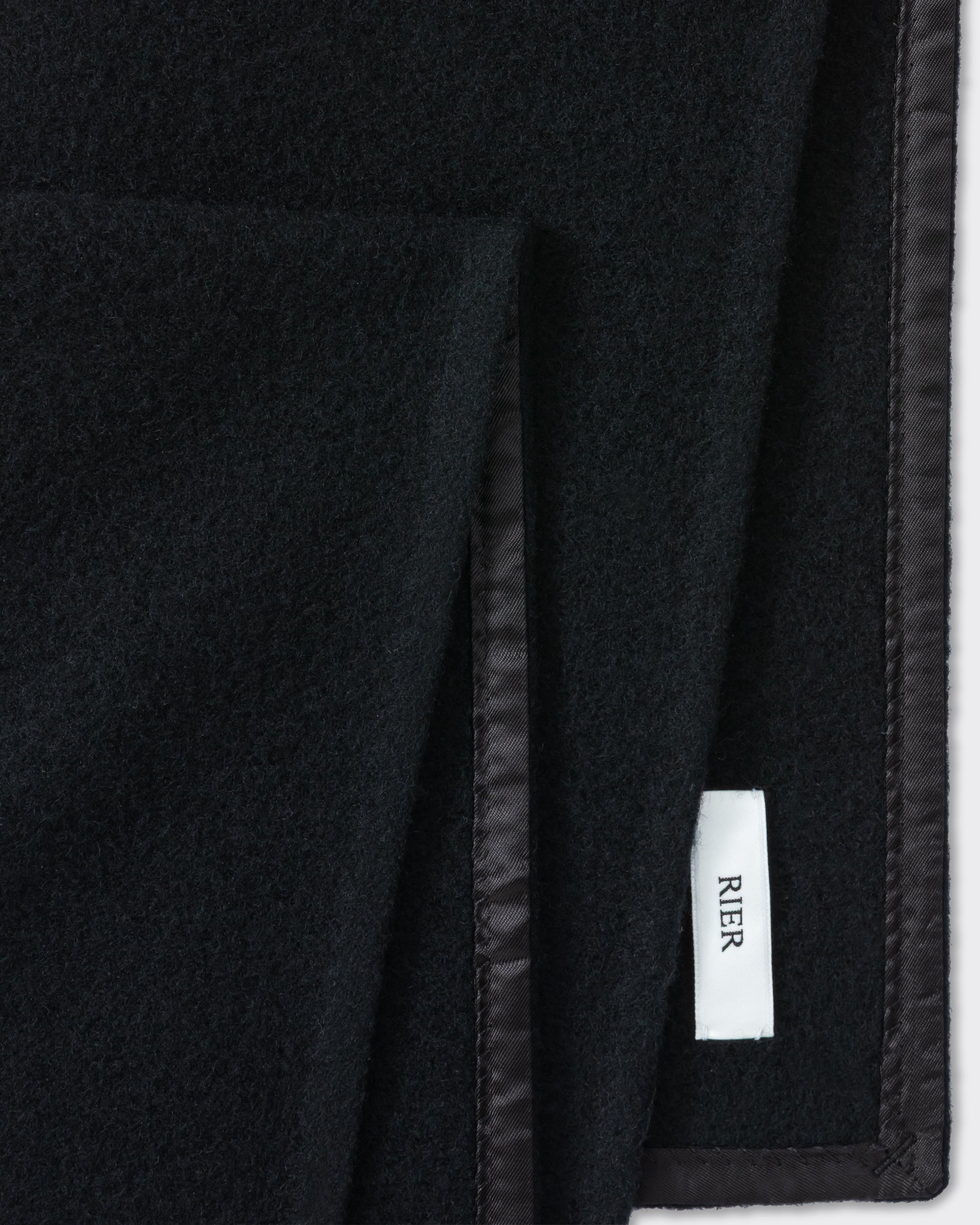 RIER wool fleece scarf in black, close-up of the finished edge and woven label