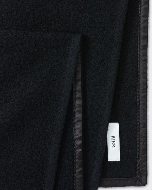 RIER wool fleece scarf in black, close-up of the finished edge and woven label