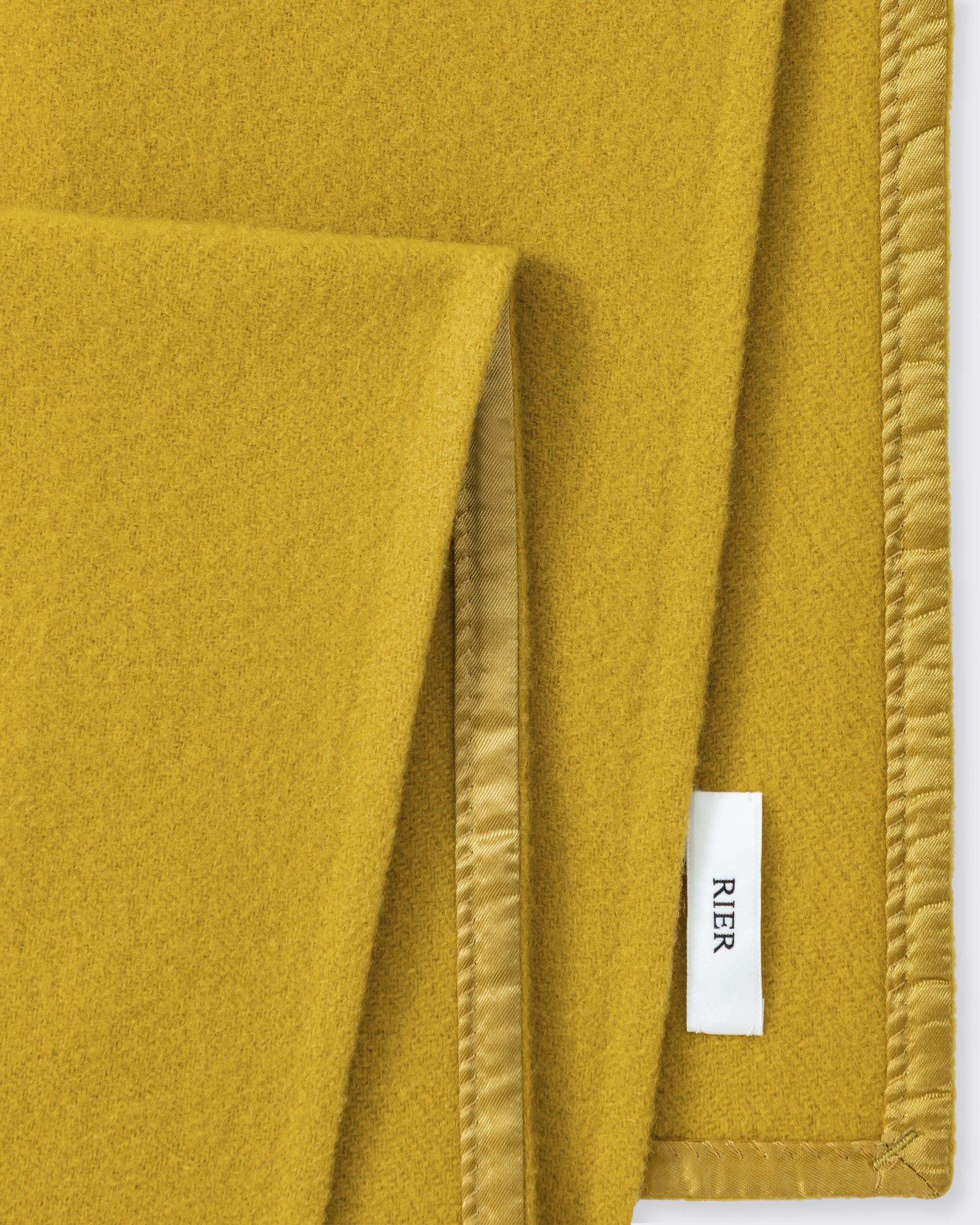 RIER wool fleece scarf in Wax mustard yellow, close-up of the finished edge and woven label